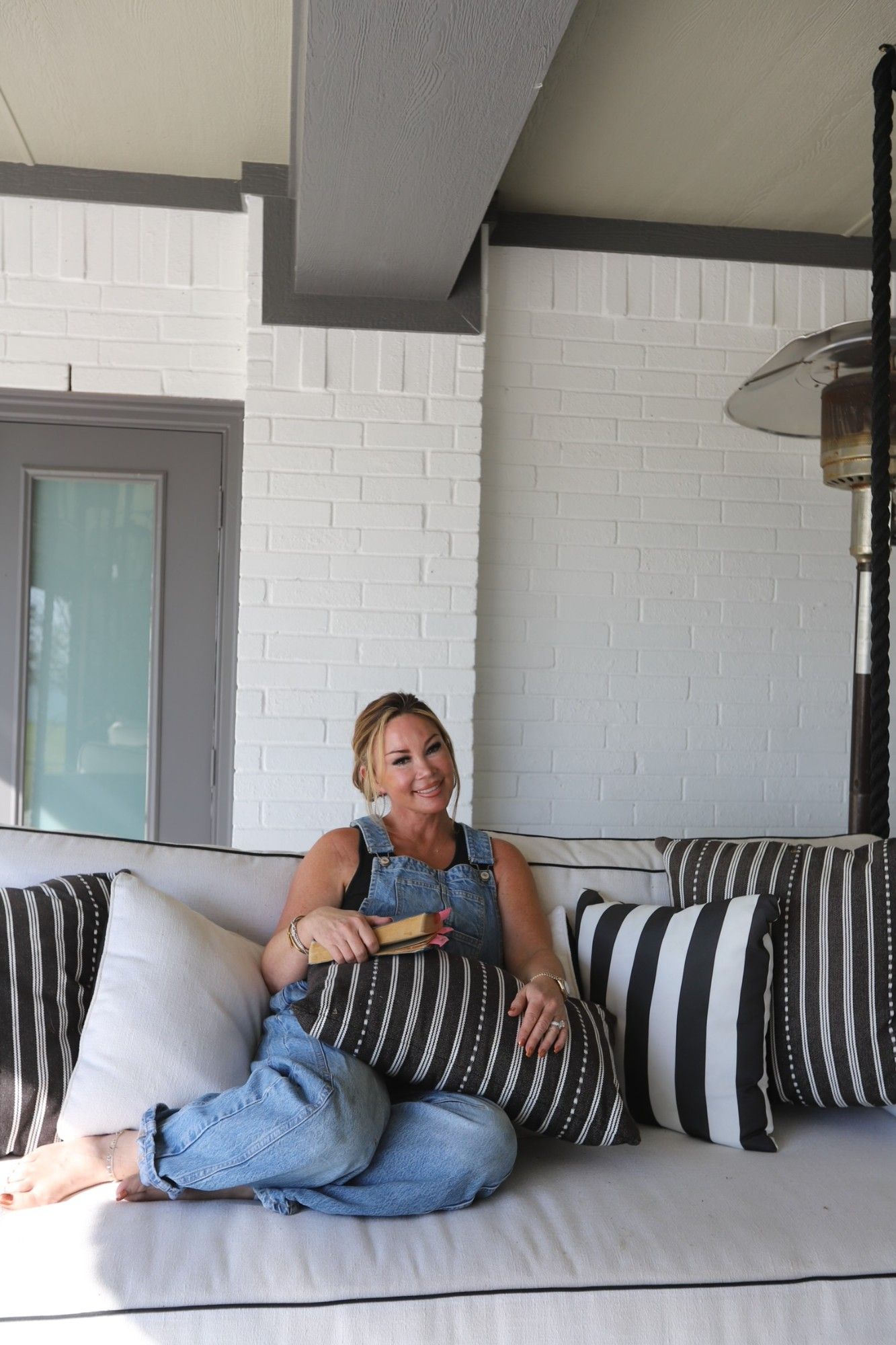 Jenn on a porch swing with a book, in denim overalls.