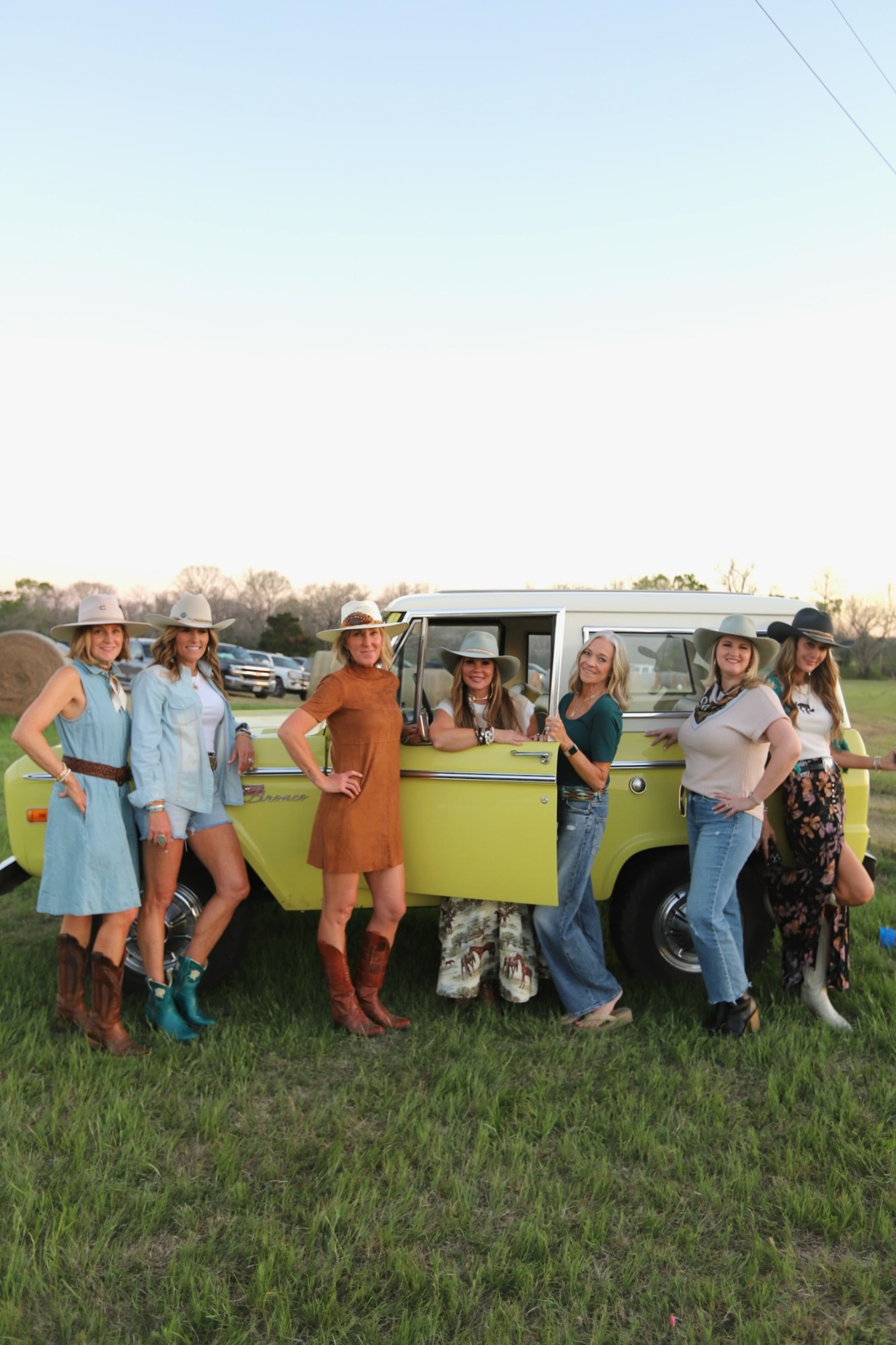 A group of women in cowboy hats with a vintage Bronco at sunset on a Texas ranch.